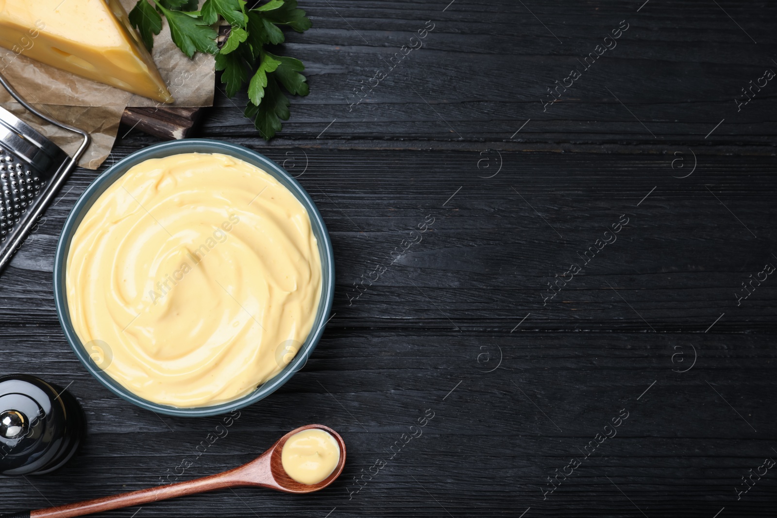 Photo of Tasty cheese sauce and parsley on black wooden table, flat lay. Space for text