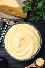 Tasty cheese sauce and parsley on black wooden table, flat lay