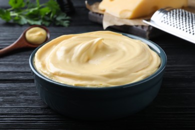 Photo of Tasty cheese sauce in bowl on black wooden table, closeup