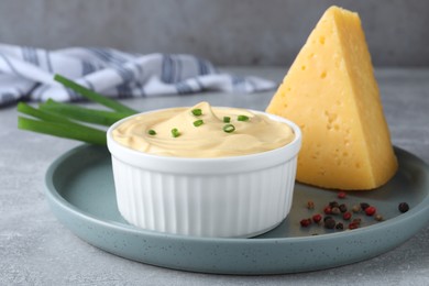 Photo of Tasty cheese sauce with green onion and peppercorns on light grey table, closeup