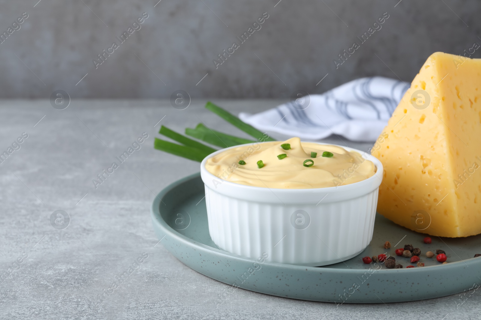 Photo of Tasty cheese sauce with green onion and peppercorns on light grey table, space for text