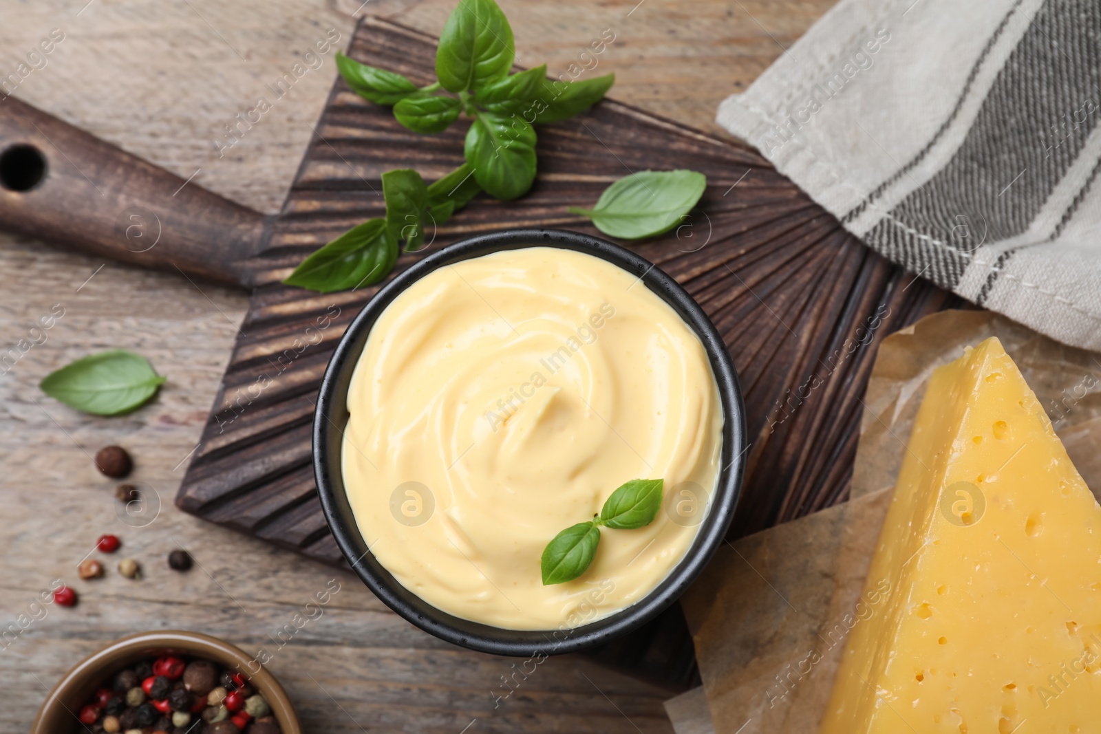 Photo of Tasty cheese sauce with basil and peppercorns on wooden table, flat lay