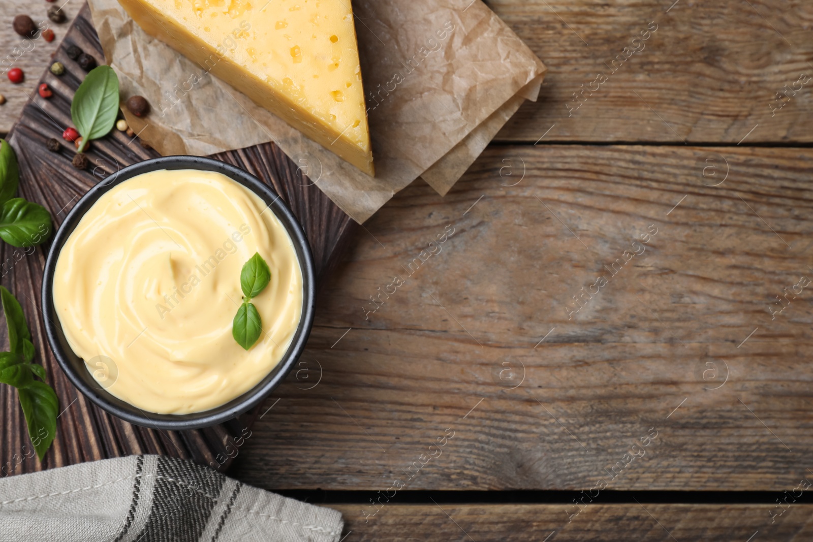 Photo of Tasty cheese sauce with basil and peppercorns on wooden table, flat lay. Space for text