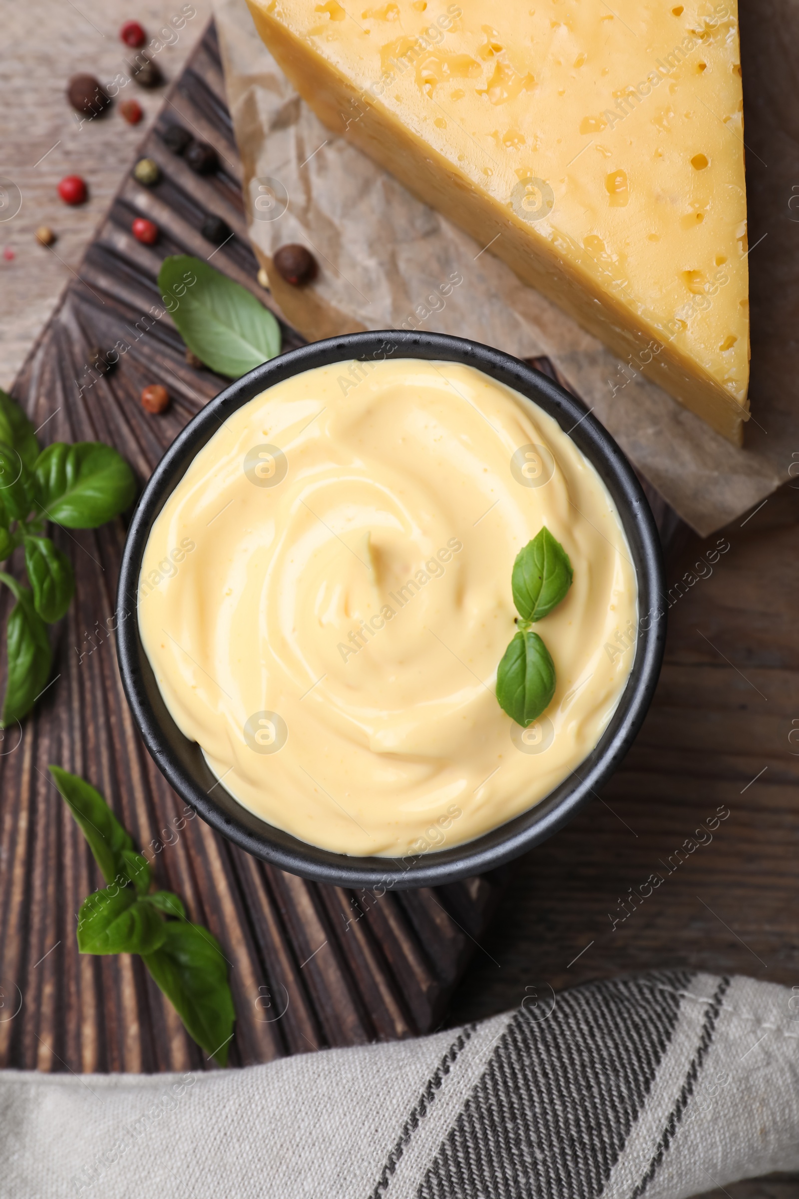 Photo of Tasty cheese sauce with basil and peppercorns on wooden table, flat lay