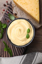 Tasty cheese sauce with basil and peppercorns on wooden table, flat lay