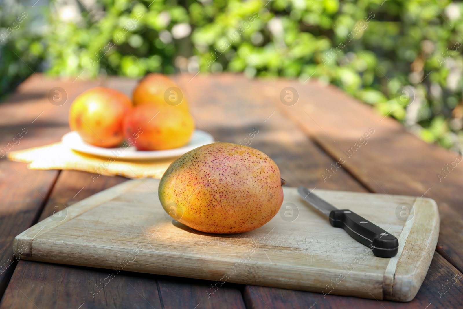 Photo of Tasty mango and knife on wooden board outdoors