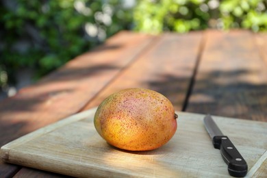 Photo of Board with tasty mango and knife on wooden table outdoors