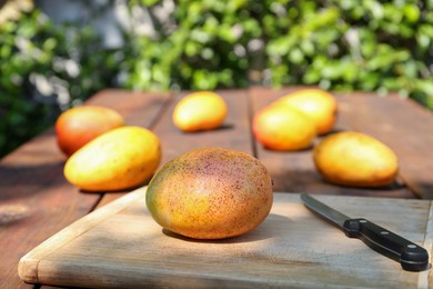 Tasty mango and knife on wooden board outdoors