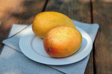 Photo of Plate with tasty mangoes on wooden table outdoors