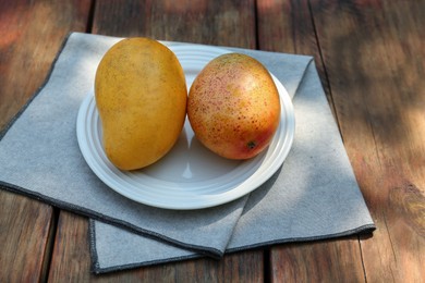 Plate with tasty mangoes on wooden table outdoors