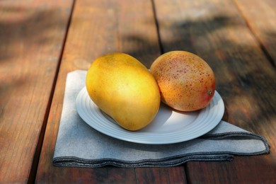 Photo of Plate with tasty mangoes on wooden table outdoors