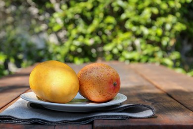 Plate with tasty mangoes on wooden table outdoors