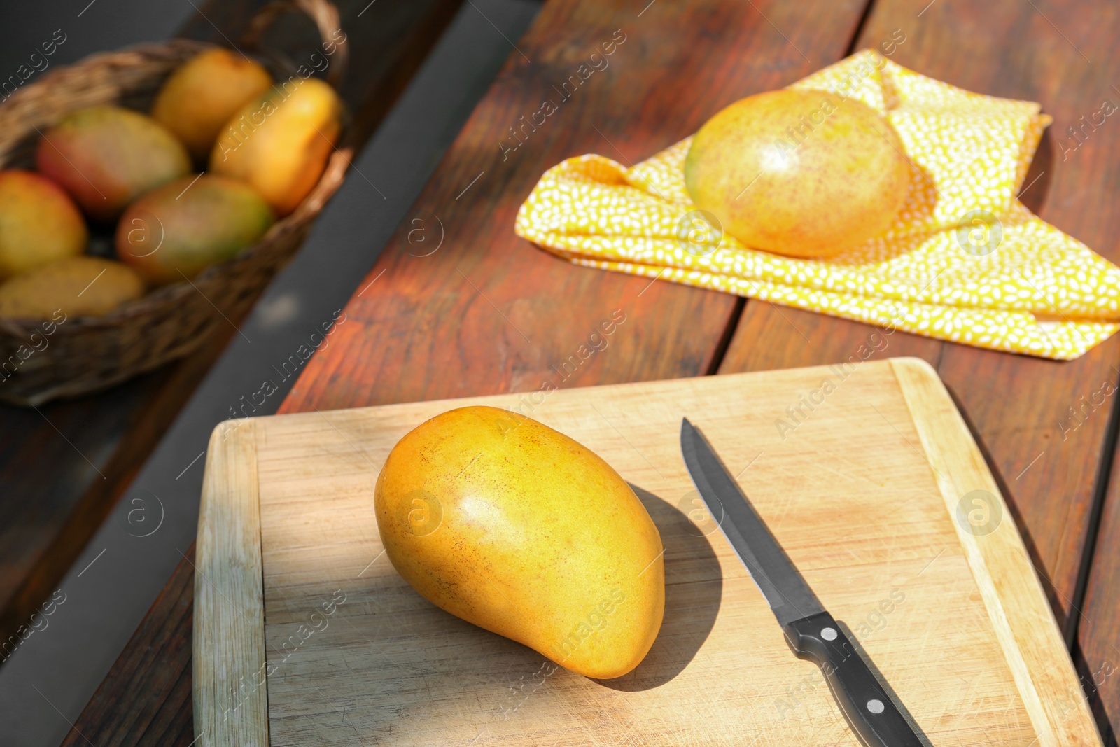 Photo of Tasty mangoes, cutting board and knife on wooden table outdoors