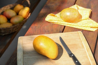 Photo of Tasty mangoes, cutting board and knife on wooden table outdoors