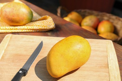 Photo of Tasty mangoes, cutting board and knife on wooden table outdoors