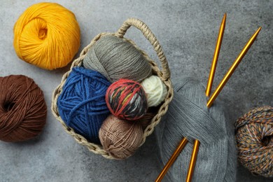 Soft woolen yarns and knitting needles on grey table, flat lay