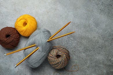 Soft woolen yarns and knitting needles on grey table, flat lay. Space for text