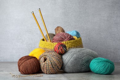 Soft woolen yarns and knitting needles on grey table