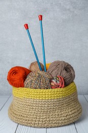 Soft woolen yarns and knitting needles on white wooden table