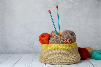 Photo of Soft woolen yarns and knitting needles on white wooden table, space for text