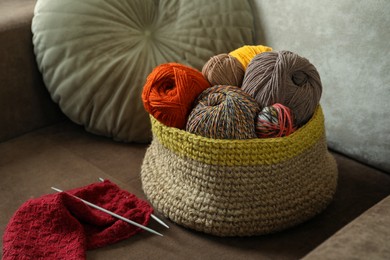 Photo of Soft woolen yarns, knitting and needles on brown sofa