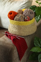 Soft woolen yarns, knitting and needles on brown sofa indoors