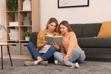 Photo of Happy mother and her teenage daughter reading book on floor at home