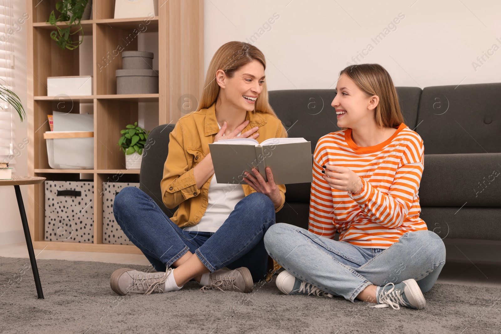 Photo of Happy mother and her teenage daughter reading book on floor at home