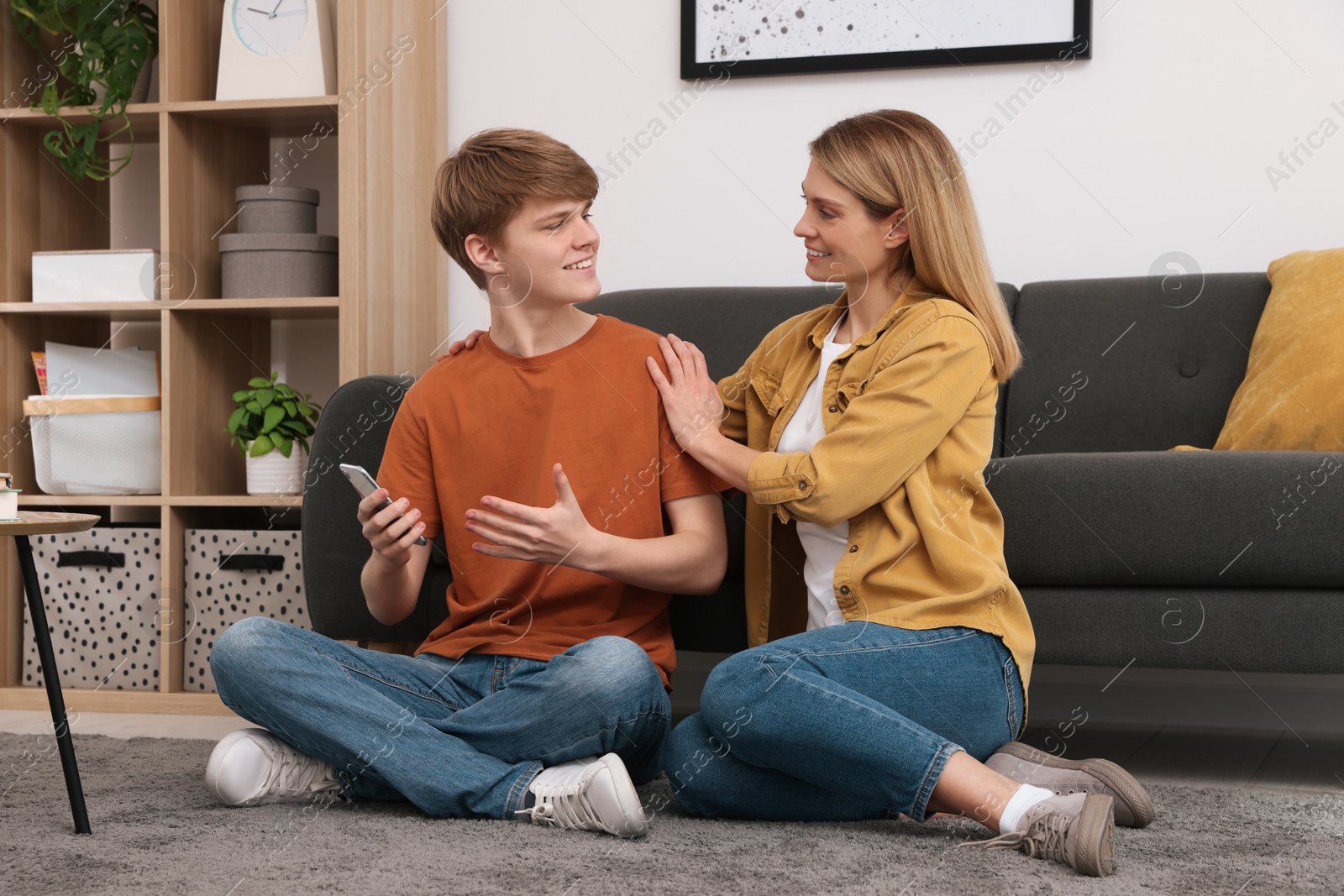 Photo of Happy mother and her teenage son spending time together on floor at home