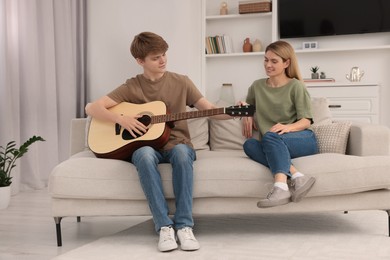 Photo of Teenage son playing guitar for his mother in living room