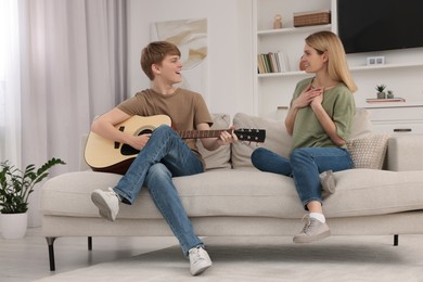 Photo of Teenage son playing guitar for his mother in living room