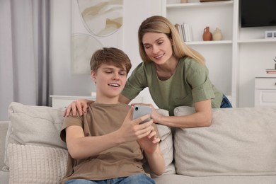 Photo of Happy mother and her teenage son with phone spending time together at home