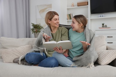 Photo of Happy mother and her teenage daughter reading book together at home