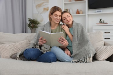 Photo of Happy mother and her teenage daughter reading book together at home