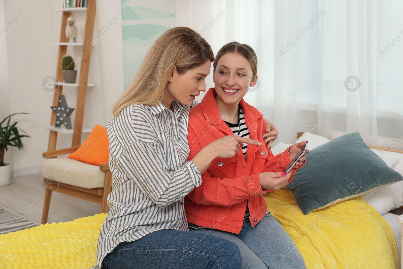 Photo of Happy mother and her teenage daughter spending time together with phone at home