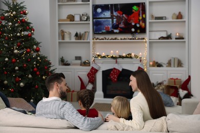 Photo of Happy family spending time on sofa near TV in cosy room, back view. Christmas atmosphere