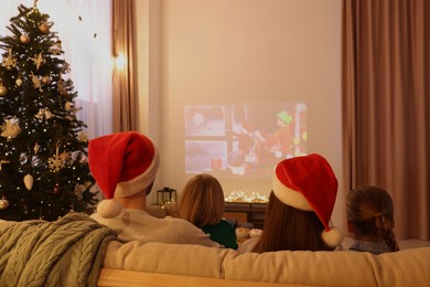 Photo of Family watching Christmas movie via video projector in cosy room, back view. Winter holidays atmosphere