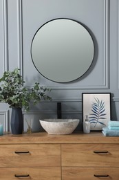 Stylish mirror over vessel sink, towels and eucalyptus branches on bathroom vanity. Interior design