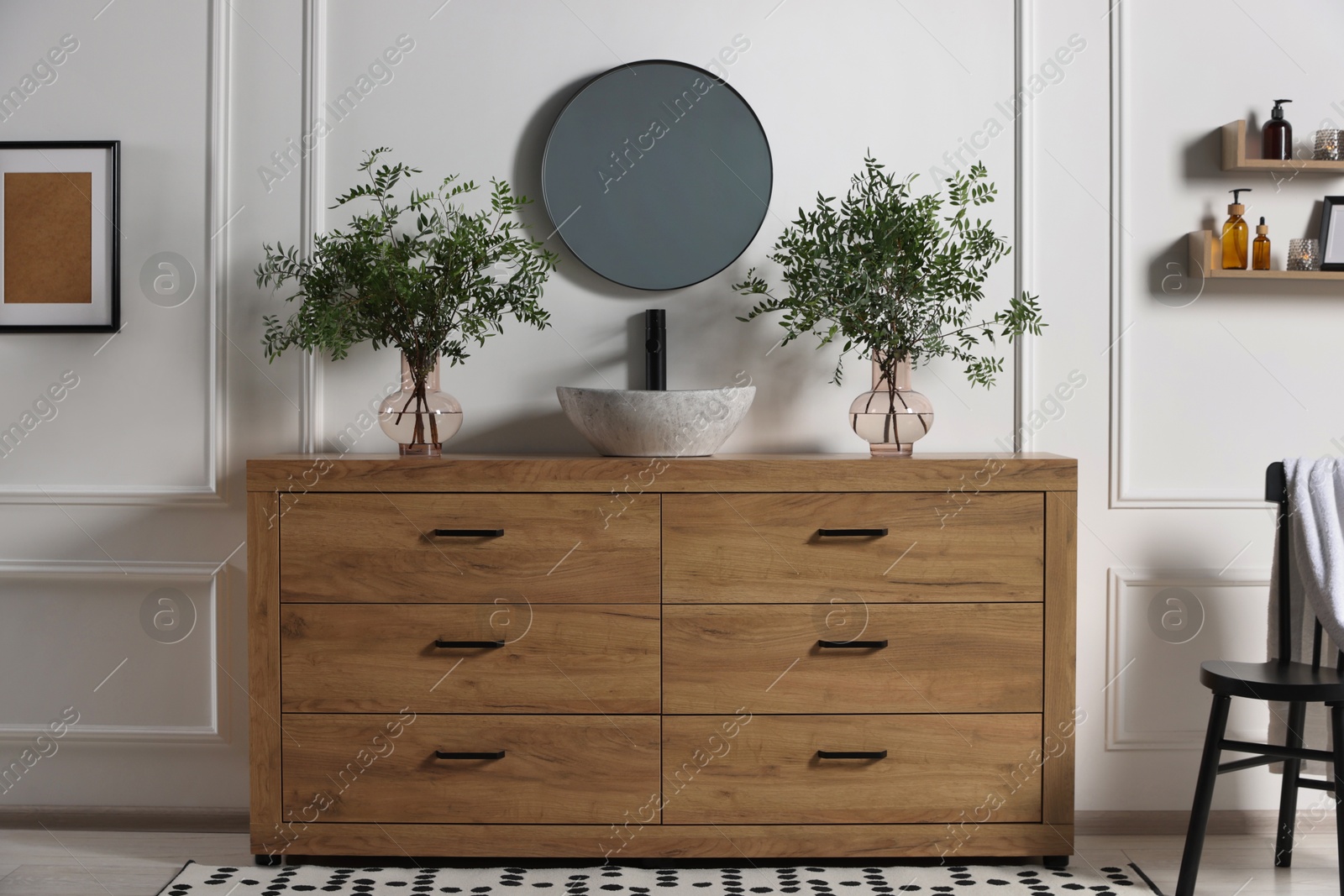 Photo of Modern bathroom interior with stylish mirror, eucalyptus branches, vessel sink and wooden vanity