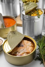 Photo of Open tin cans with salmon and different products on white table, closeup