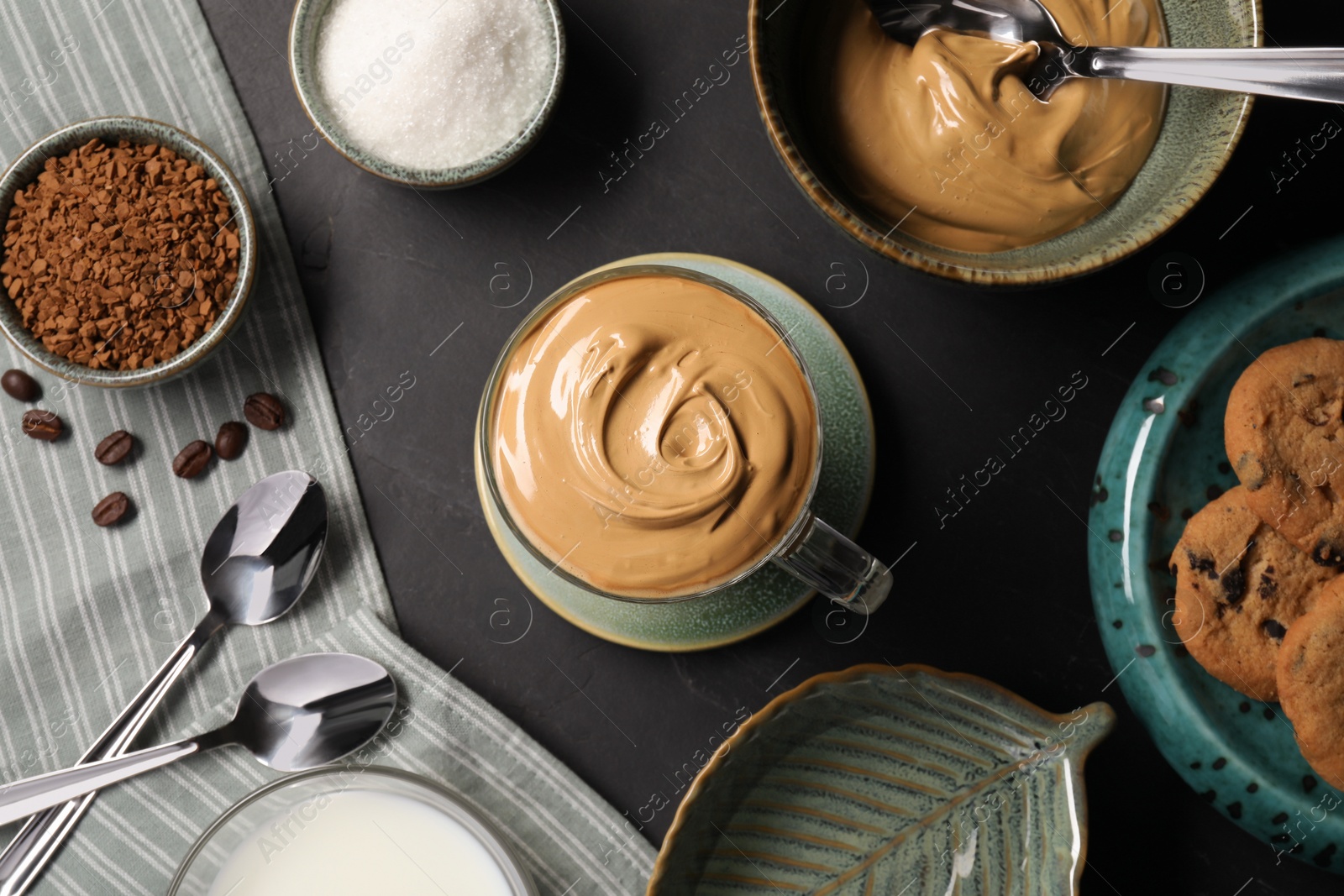 Photo of Glass mug of delicious dalgona coffee and ingredients on dark table, flat lay