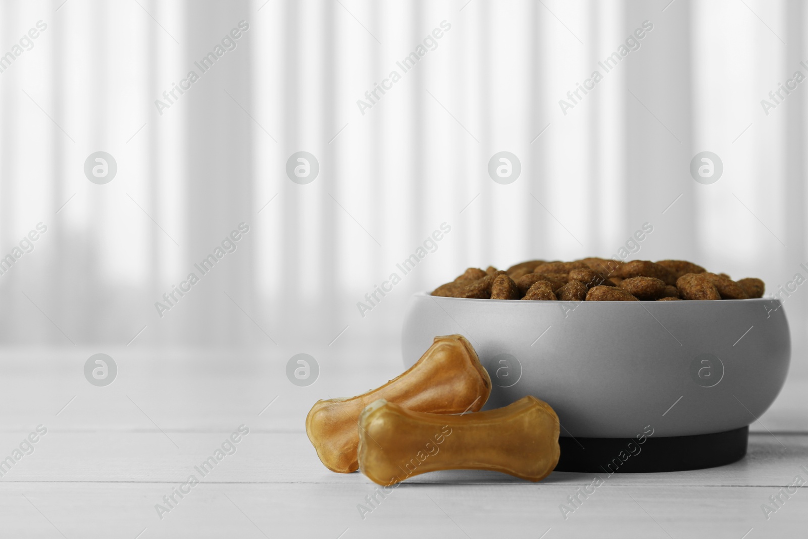 Photo of Chew bones and dry dog food on white wooden surface indoors, space for text