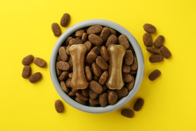 Chew bones and dry dog food on yellow background, flat lay