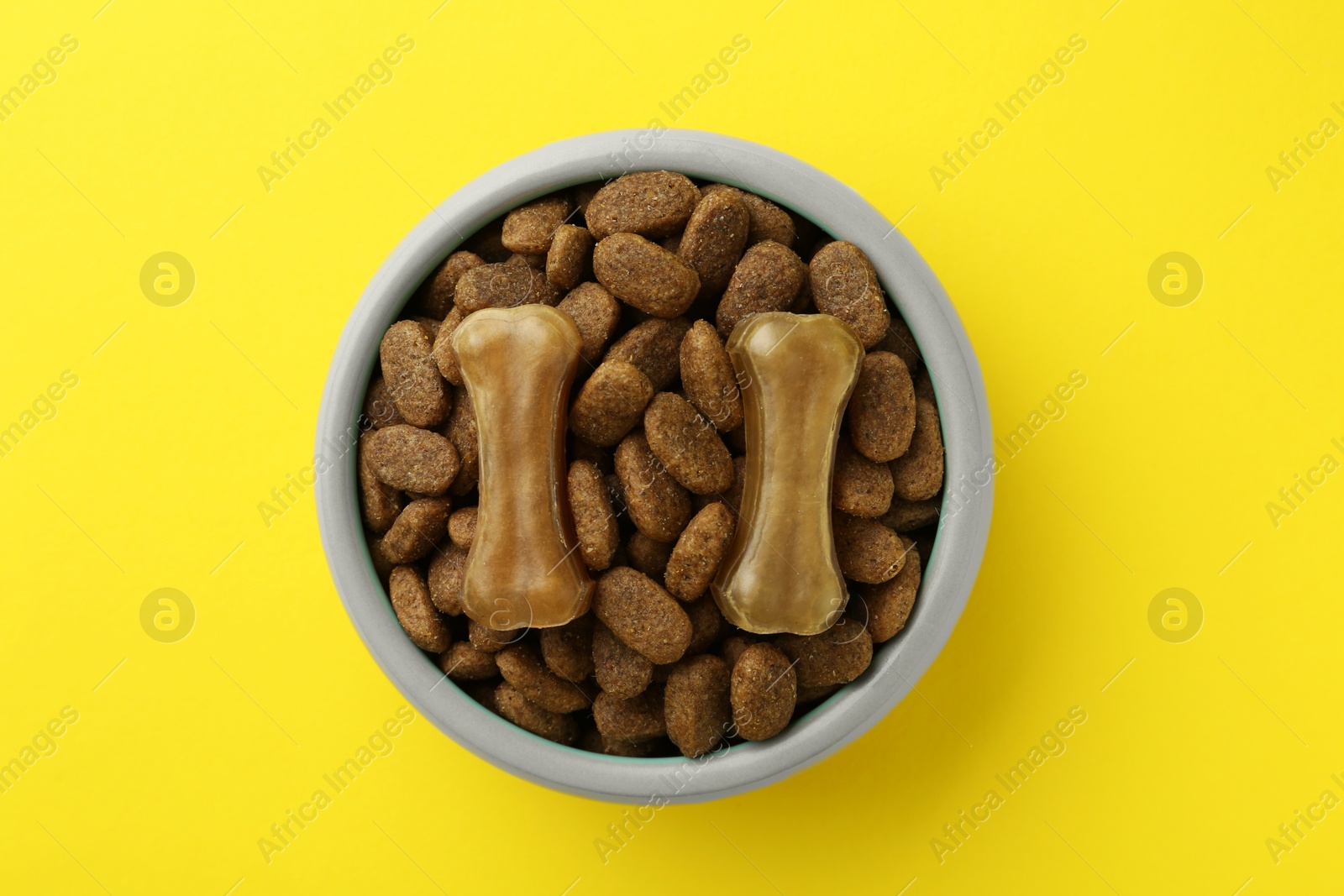 Photo of Chew bones and dry dog food on yellow background, top view