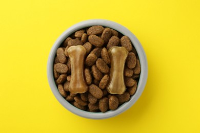 Chew bones and dry dog food on yellow background, top view