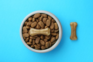 Chew bones and dry dog food on light blue background, flat lay