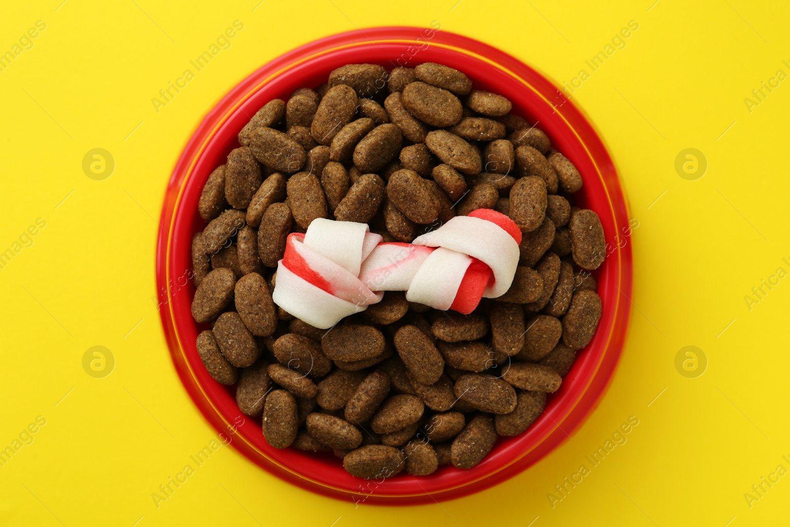 Photo of Chew bone and dry dog food on yellow background, top view