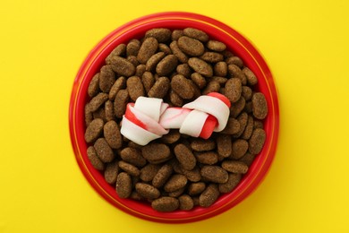 Chew bone and dry dog food on yellow background, top view