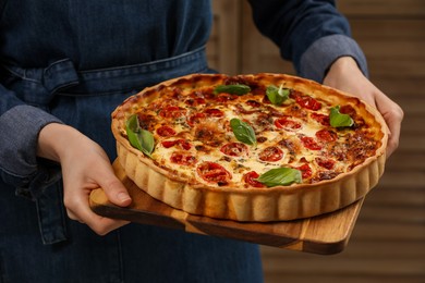 Woman holding delicious homemade quiche with prosciutto against wooden folding screen, closeup