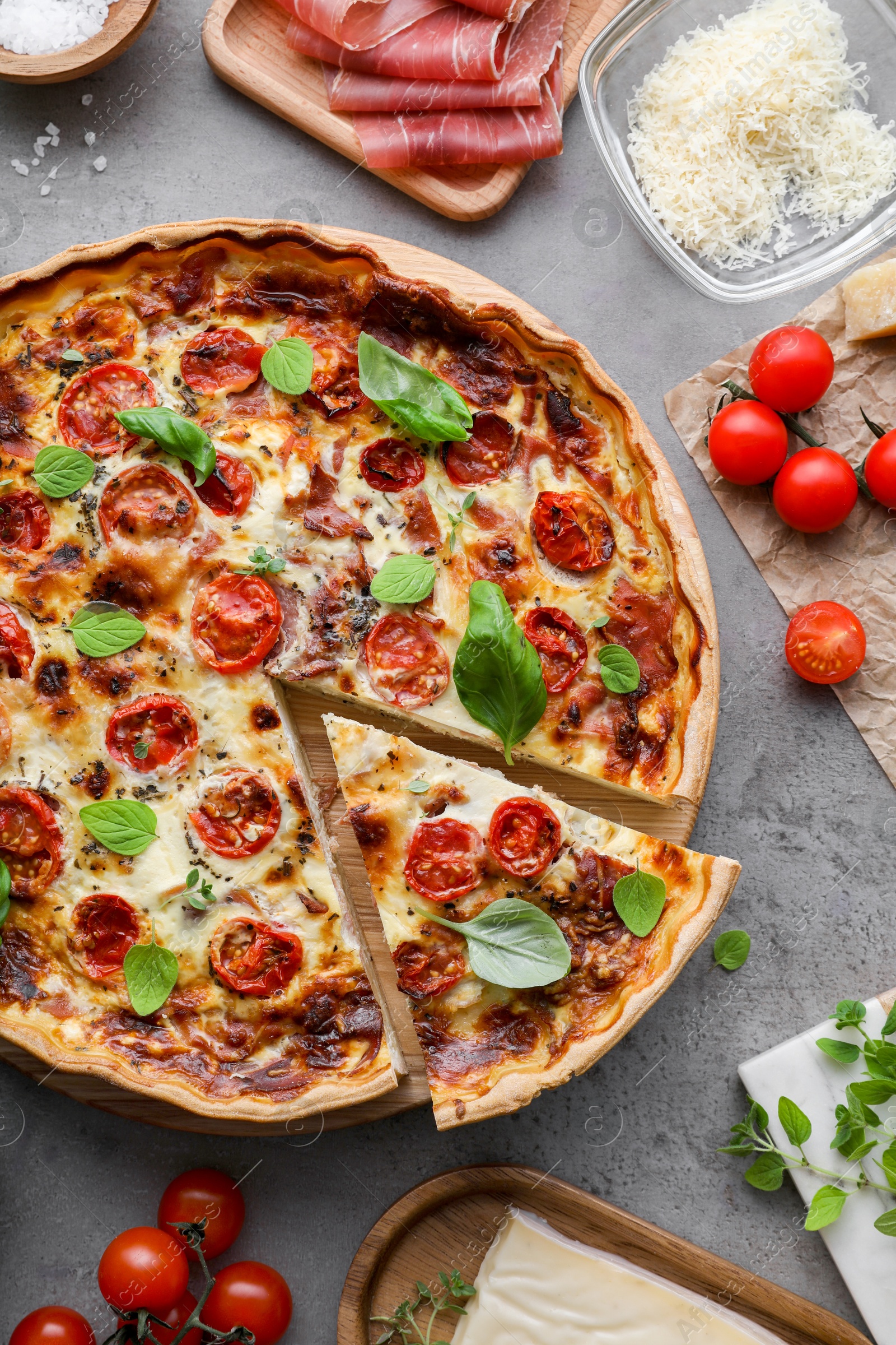 Photo of Cut delicious homemade quiche with prosciutto and ingredients on light grey table, flat lay